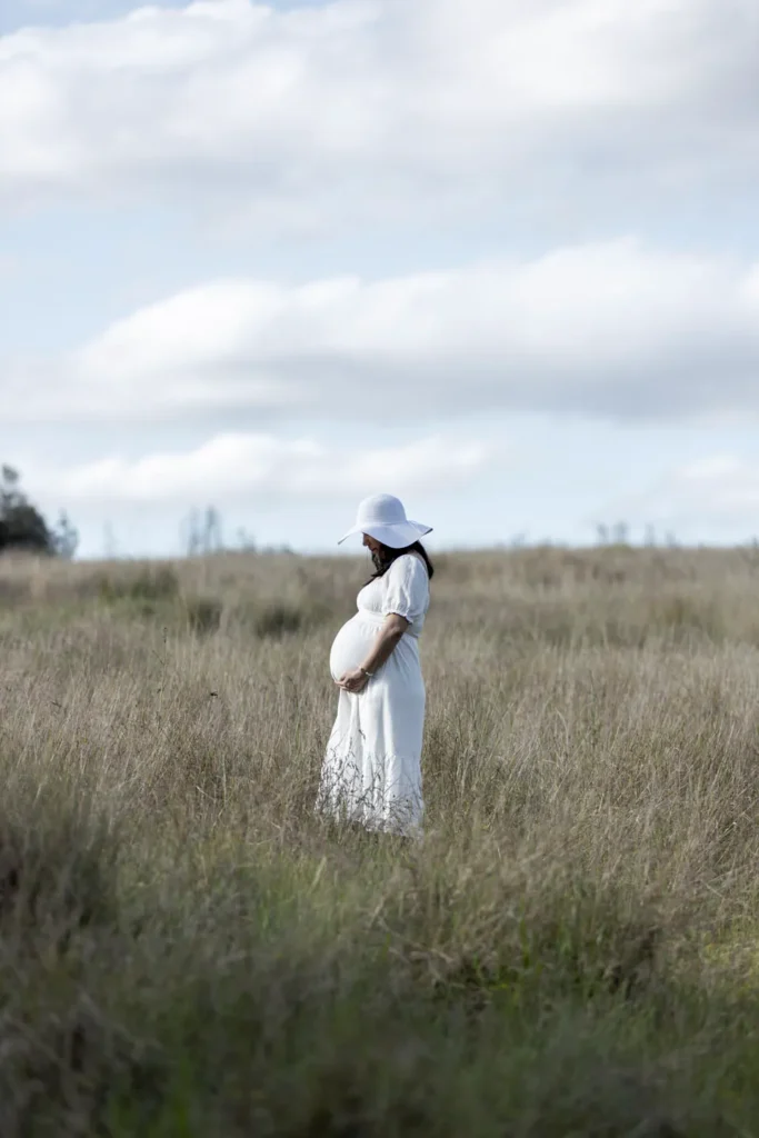 Pregnant woman standing in an open field during an outdoor maternity photography session