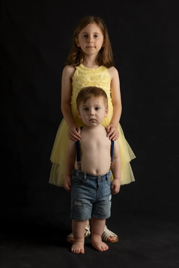 Young brother and sister photographed together against a dark studio background
